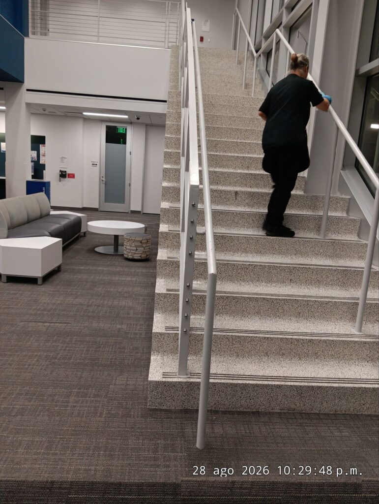Caring Commercial Cleaning team member sanitizing a staircase handrail in a Houston office building
