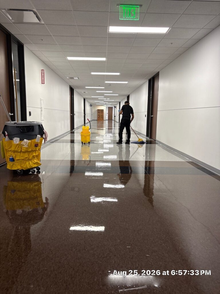 Caring Janitorial Services technician wet-mopping a freshly cleaned, high-gloss commercial office hallway floor with a yellow mop bucket and janitorial cart in Houston, Texas