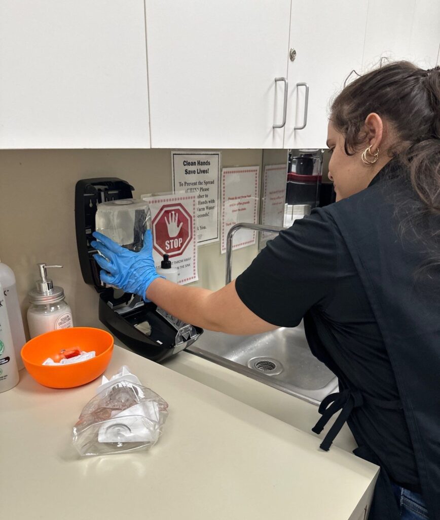 Caring Commercial Cleaning day porter restocking a soap dispenser in an office building break room